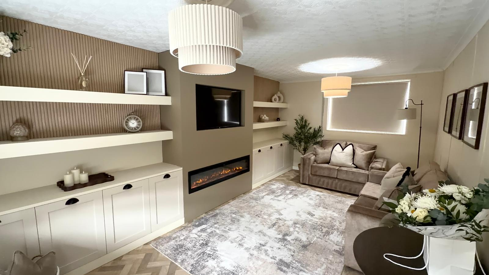 A beautifully transformed living room with built-in shelving, electric fireplace, soft neutral furnishings and warm lighting